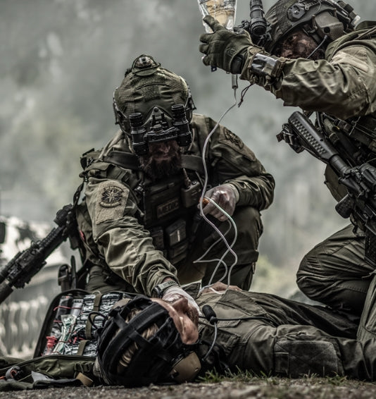 Combat medics with IV bag treating wounded soldier